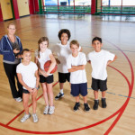 Multi-ethnic elementary or middle school students in school gym with coach playing basketball.