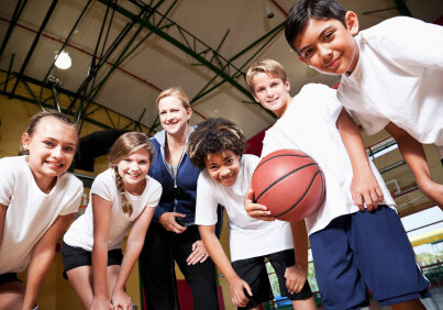 Multi-ethnic elementary or middle school students in school gym with coach playing basketball.